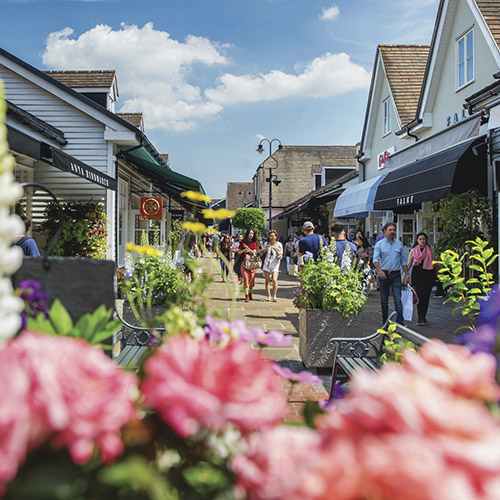 Bicester Village in the summer with flowers in the foreground and people shopping in the background