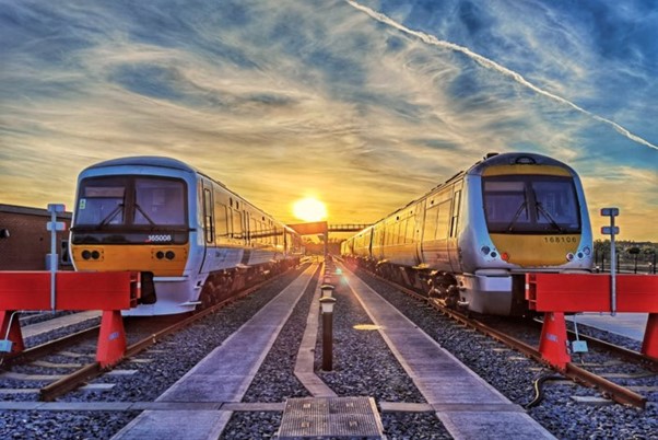 Two Chiltern Railways trains stationed in rail sidings with sun rising behind.