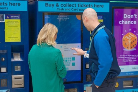 Member of staff helping a customer use a ticket vending machine
