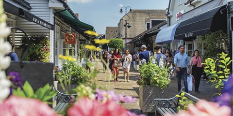 Bicester Village in the summer with flowers in the foreground and people shopping in the background